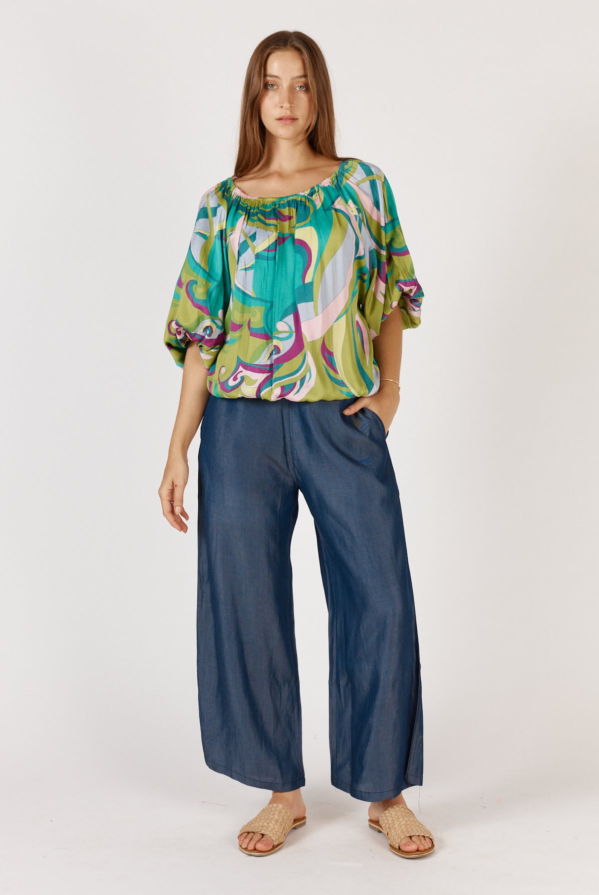Woman wearing a colorful blouse and blue pants on a white background
