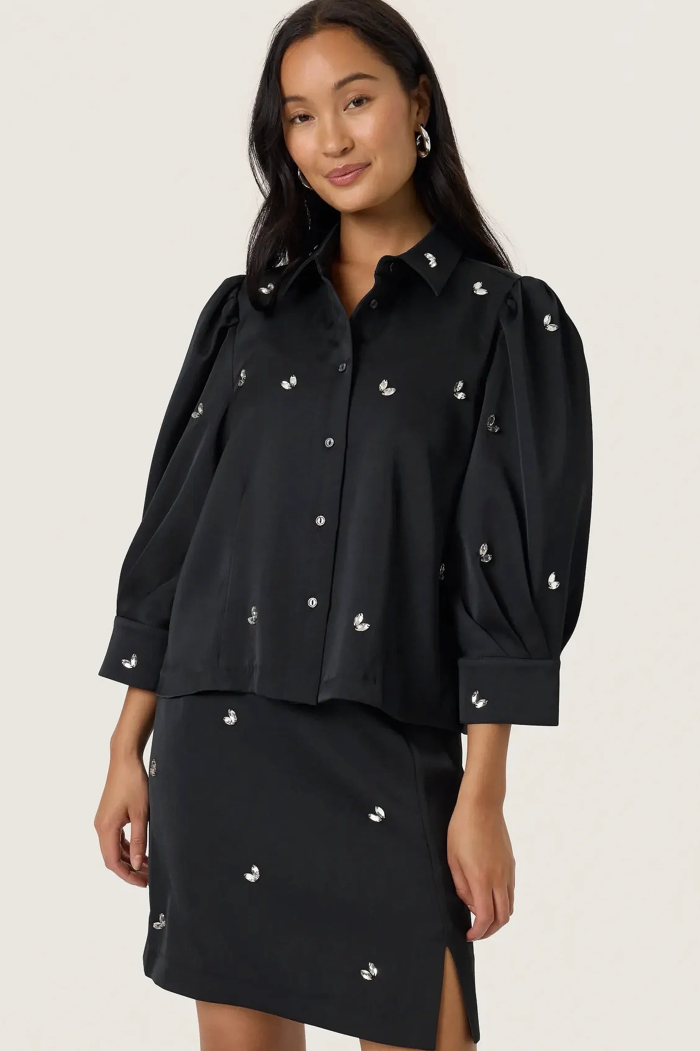 Woman wearing a black outfit with decorative elements on a plain background