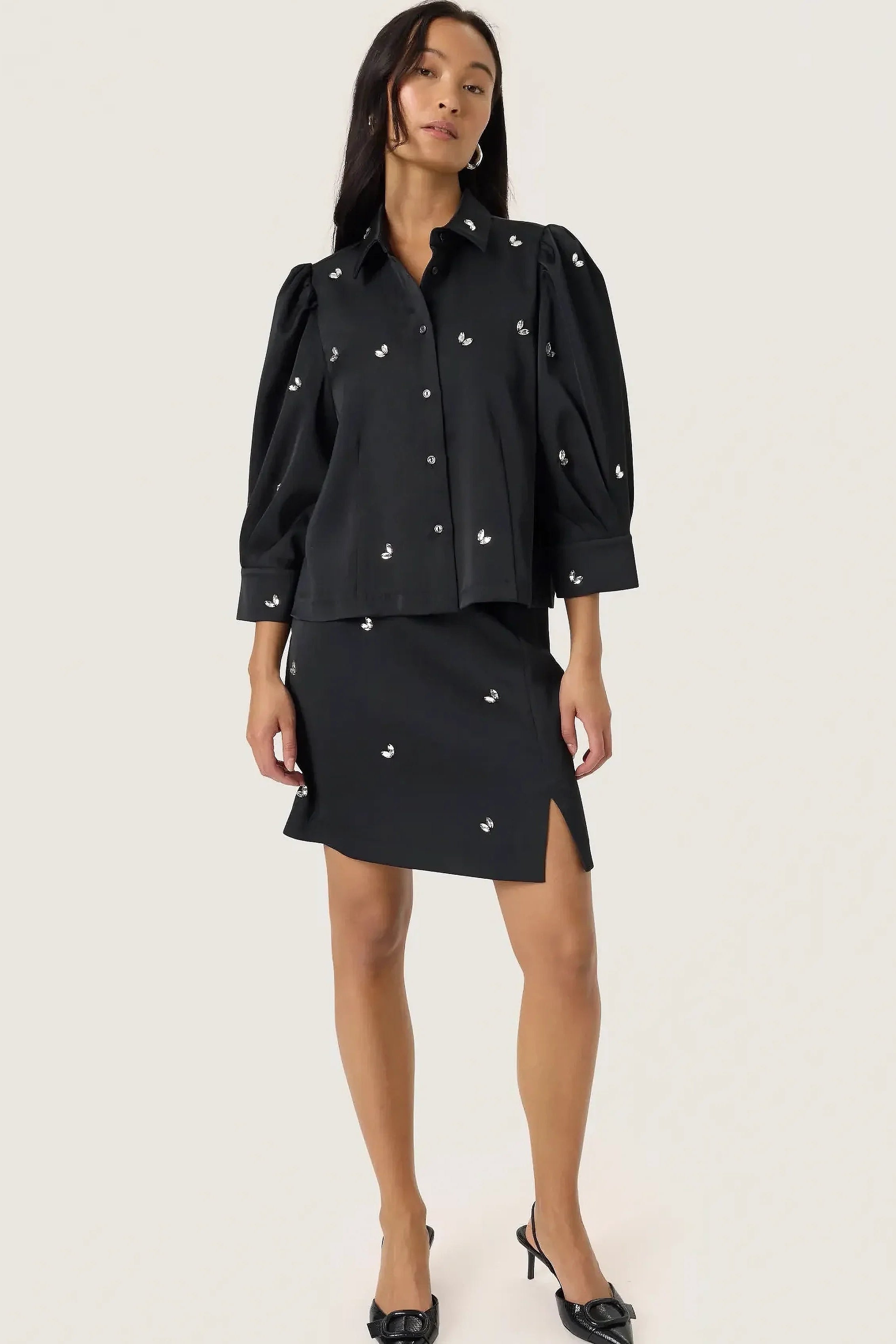 Woman wearing a black outfit with pearl embellishments on a white background