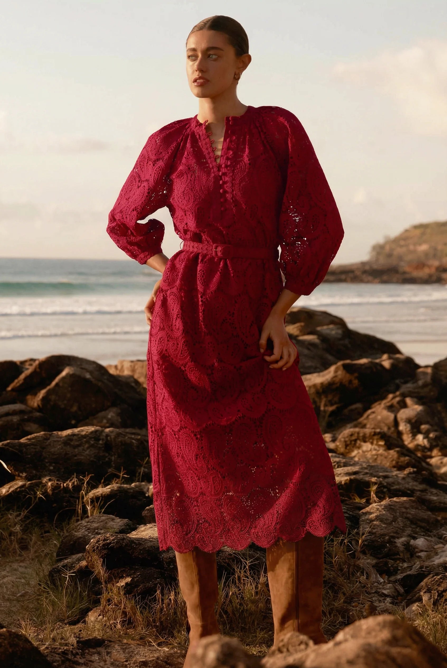 Woman in a red dress standing on a rocky beach with ocean and sky in the background