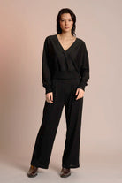 Woman wearing a black jumpsuit against a beige background