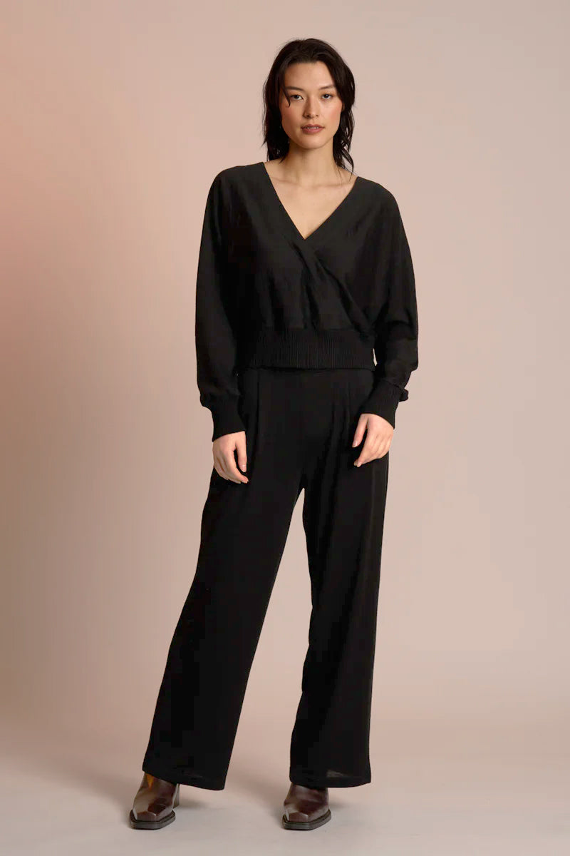 Woman wearing a black jumpsuit against a beige background