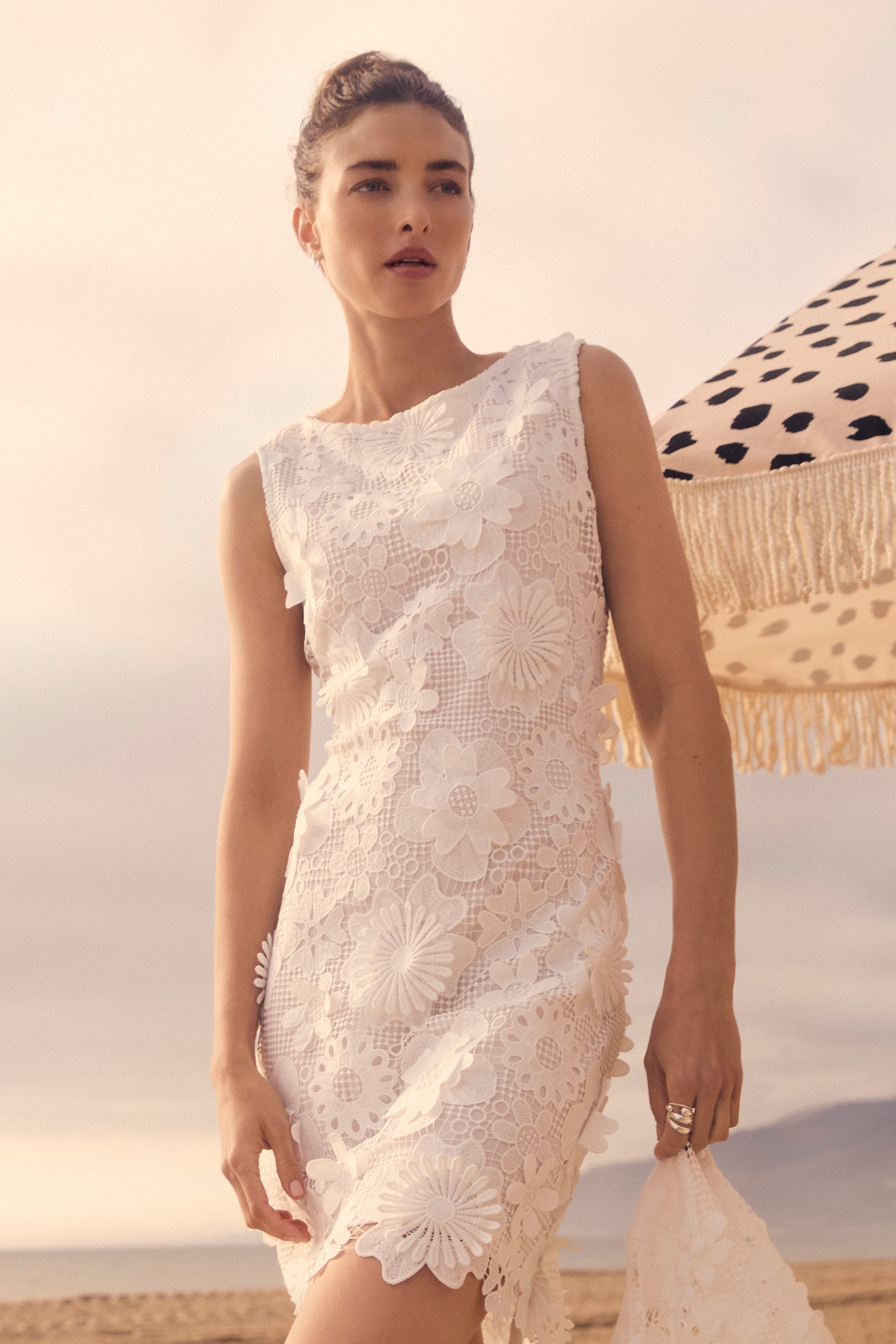 Woman in a white lace dress standing on a beach with a sunset in the background