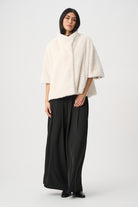 Woman wearing a white poncho and black pants on a white background