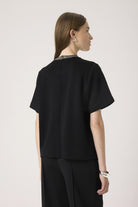 Woman wearing a black outfit with a plain background back angle