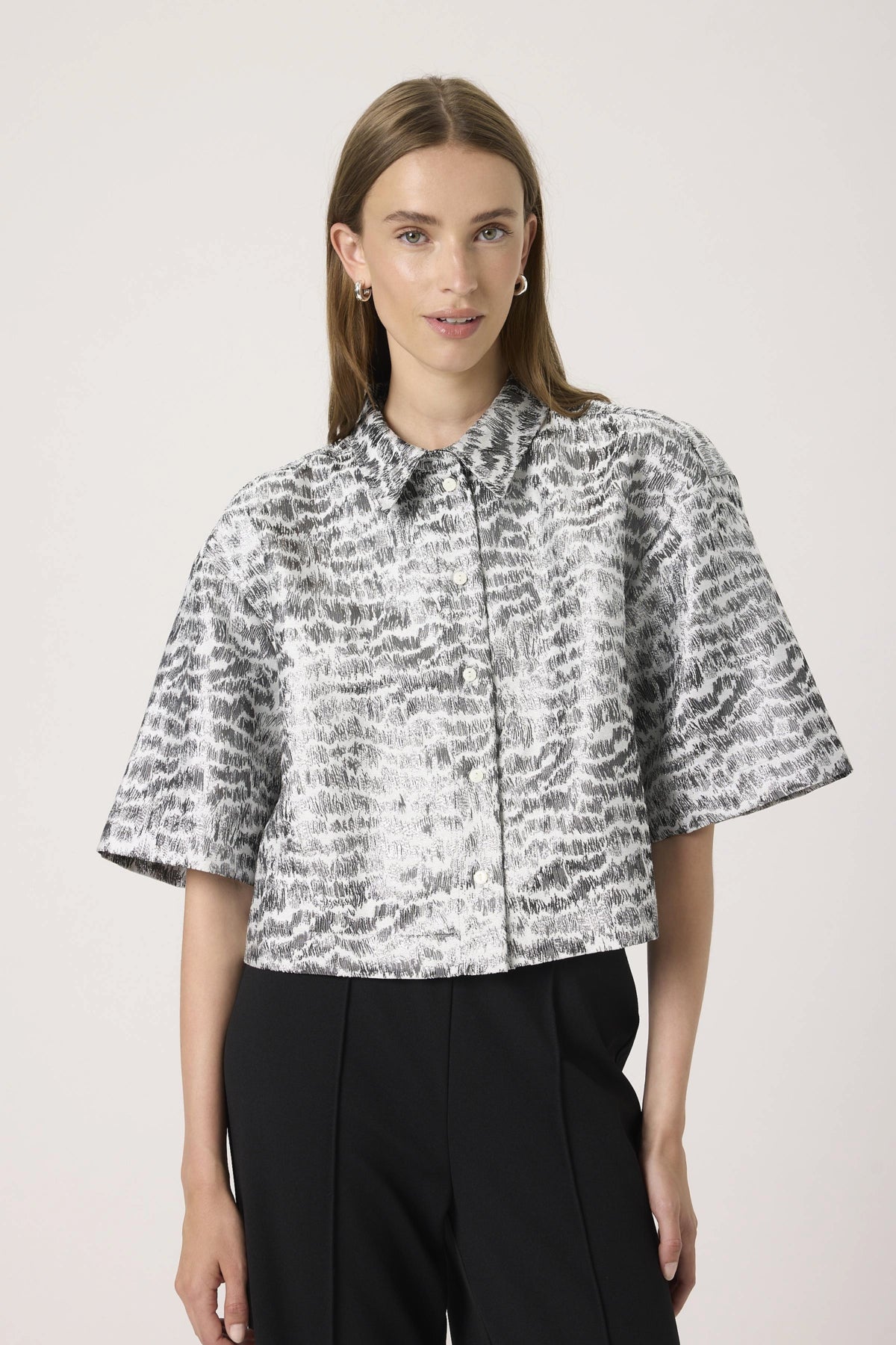Woman wearing a patterned blouse and black pants against a light background