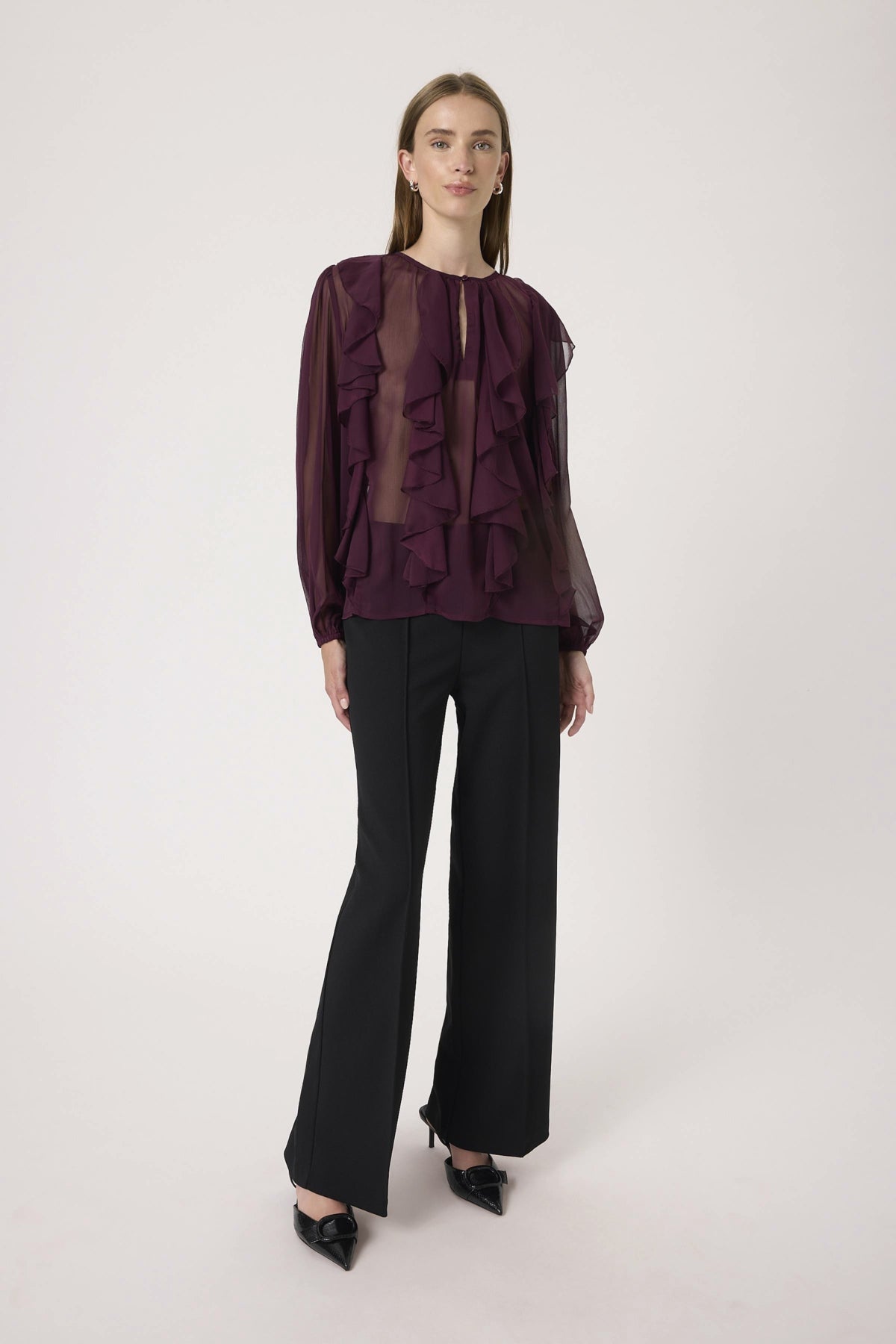 Woman wearing a dark purple ruffled blouse and black pants on a white background