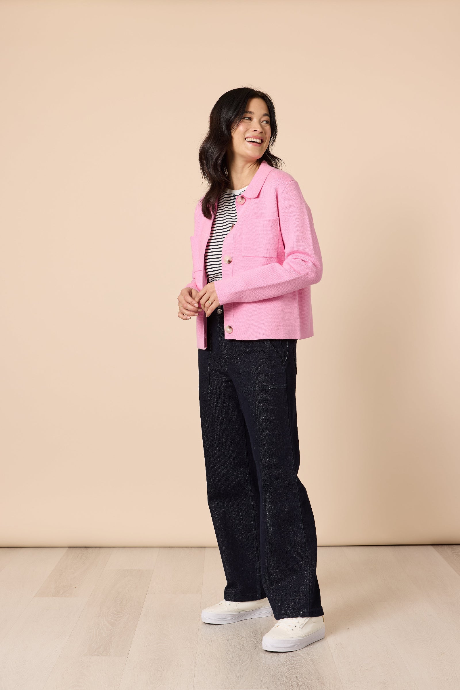 Woman wearing a pink jacket, black pants, and white shoes on a beige background