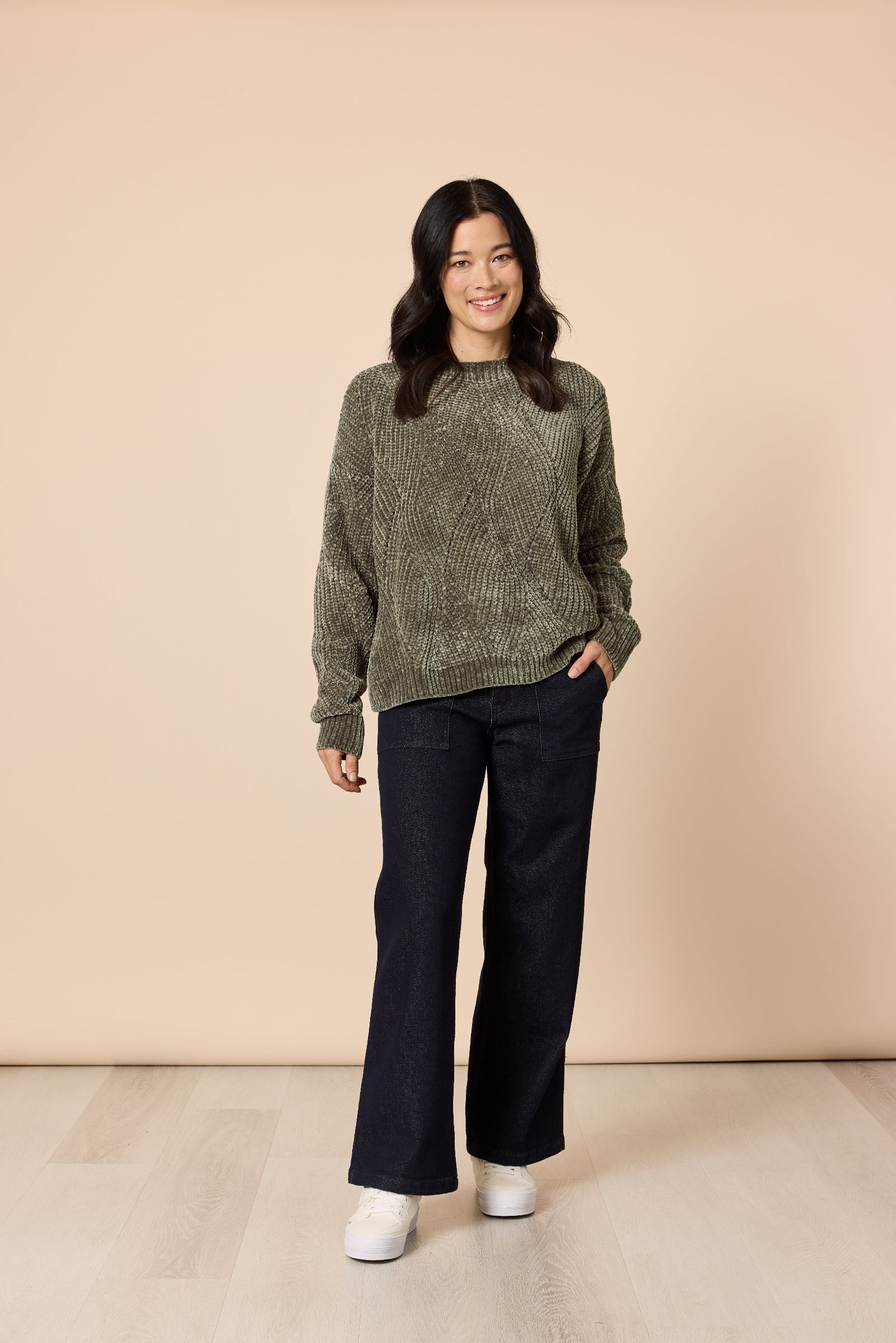 Woman wearing a green patterned sweater and black pants against a beige background