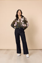 Woman wearing a floral blouse and black pants against a beige background
