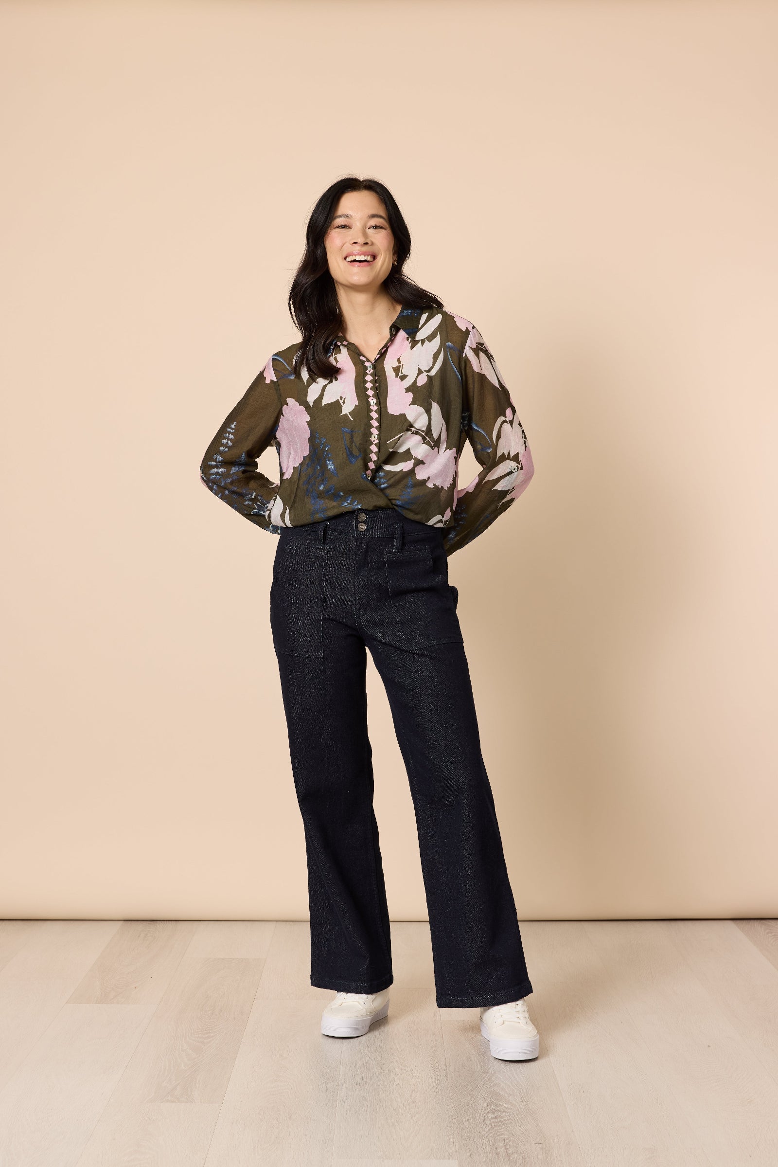 Woman wearing a floral blouse and black pants against a beige background