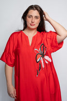 Woman wearing a v neck bright red midi length dress with elbow length sleeves and  flower motif against a white background.