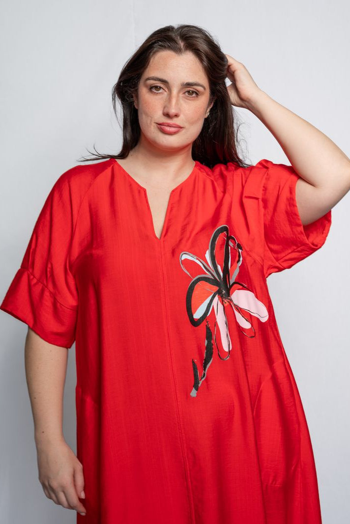 Woman wearing a v neck bright red midi length dress with elbow length sleeves and  flower motif against a white background.