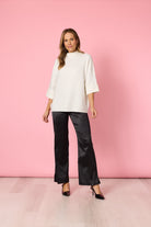 Woman wearing a white top and black pants against a pink background