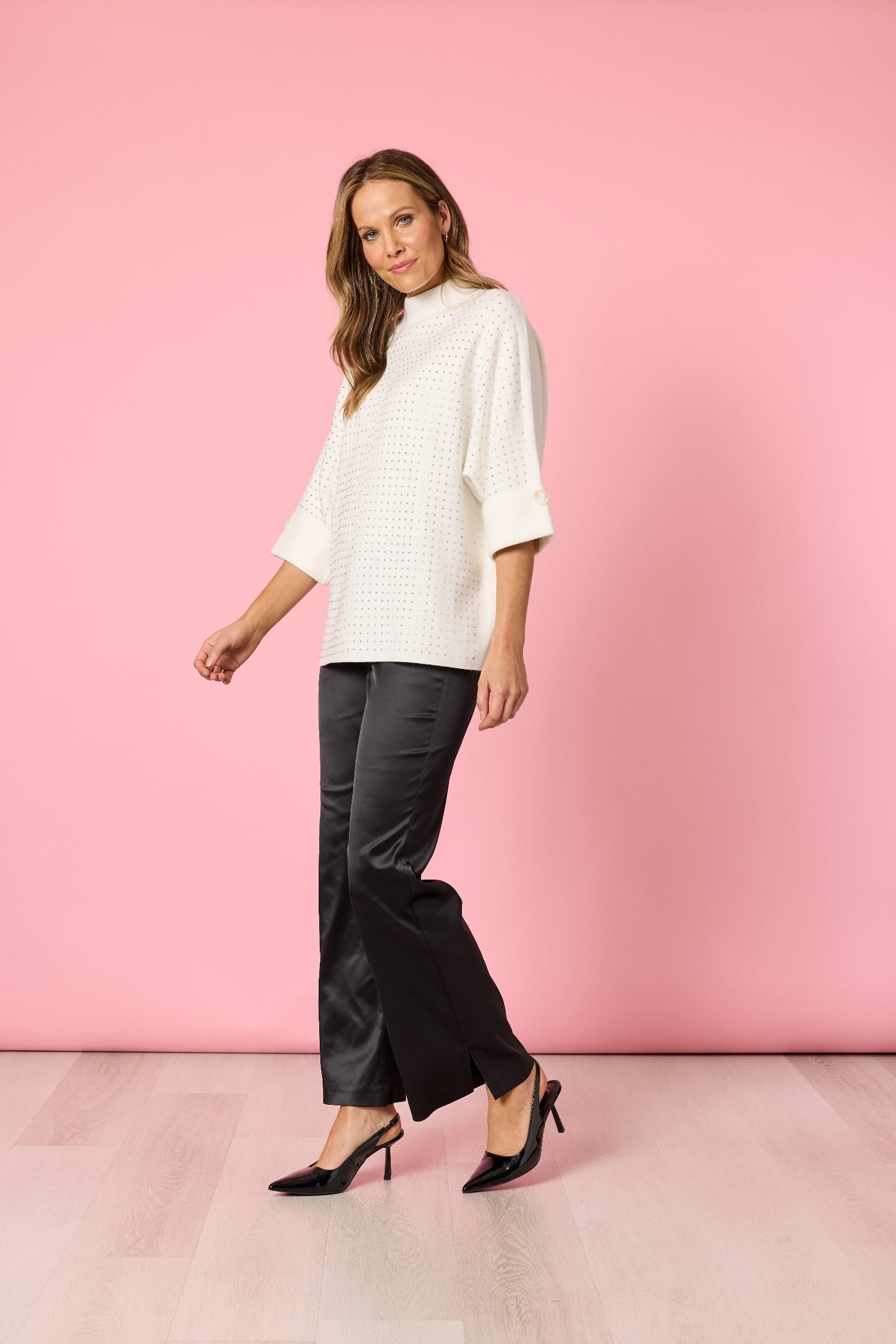 Woman wearing a white top and black pants against a pink background