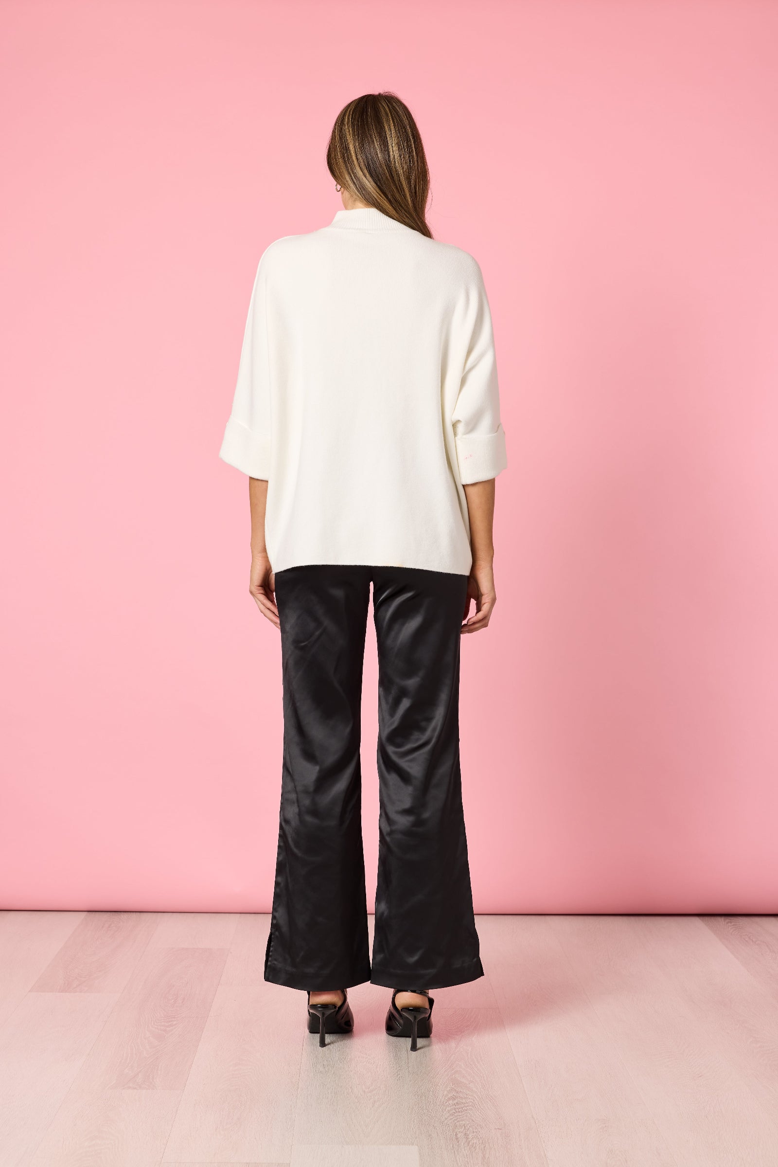 Person wearing a white shirt and black pants against a pink wall