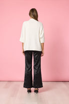 Person wearing a white shirt and black pants against a pink wall