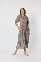 A woman modeling a leopard-print midi dress with puff sleeves and a V-neckline, standing against a plain light gray studio background.