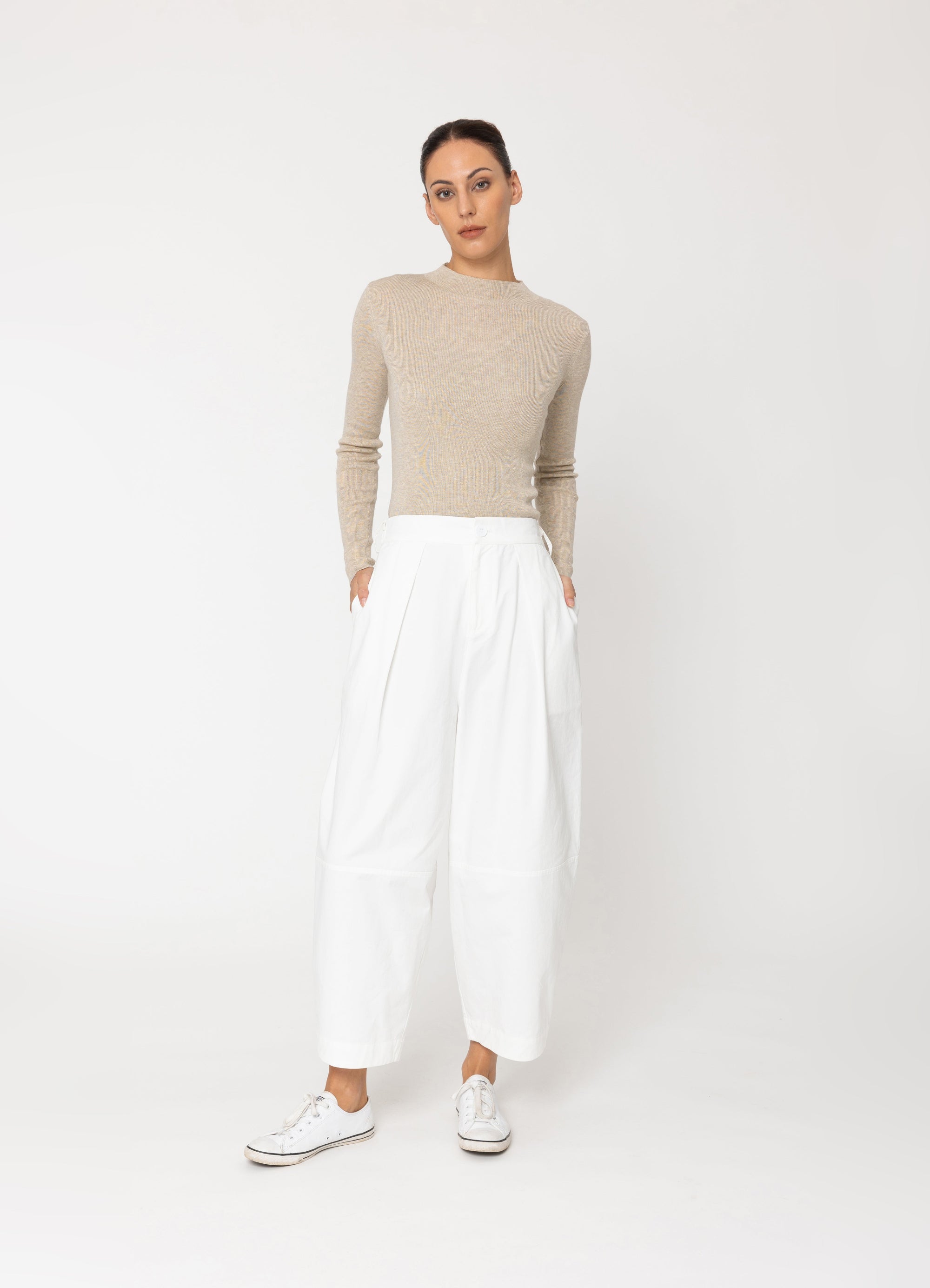 woman wearing beige top and white pants on white background