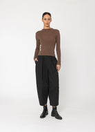 Woman wearing a brown sweater and black pants on a white background