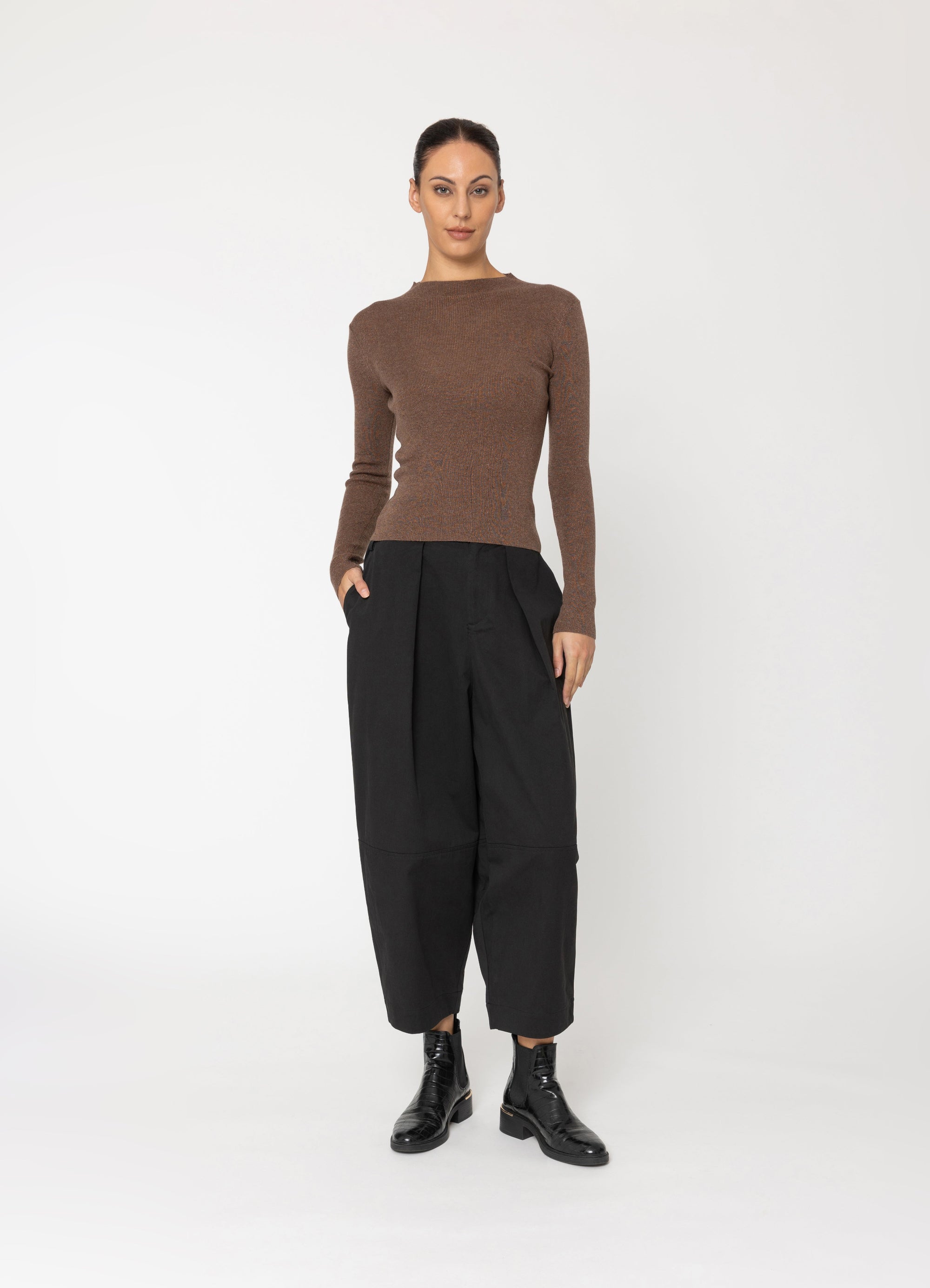 Woman wearing a brown sweater and black pants on a white background