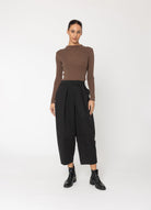 model wearing brown top and black pants on a white background