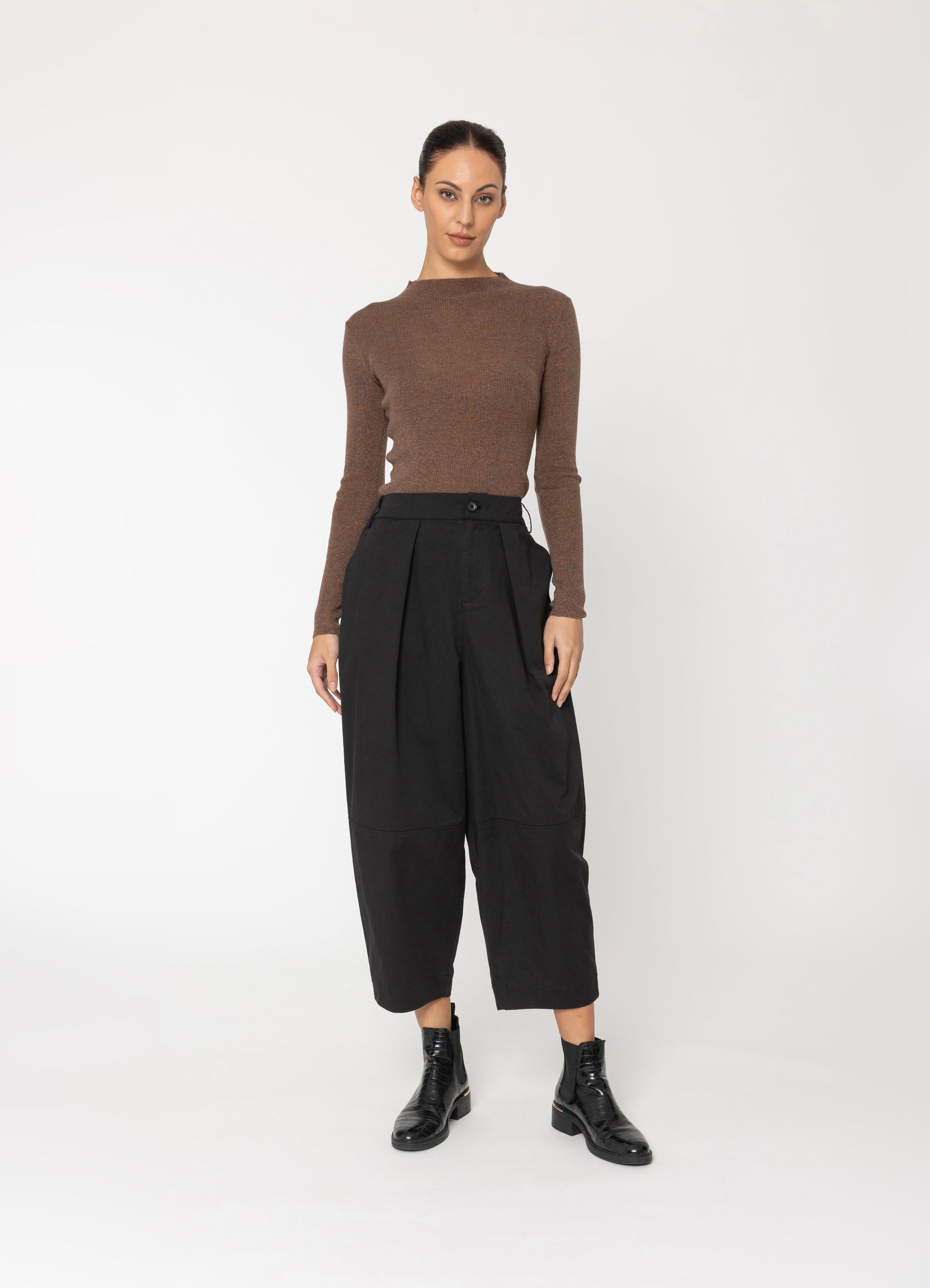 model wearing brown top and black pants on a white background