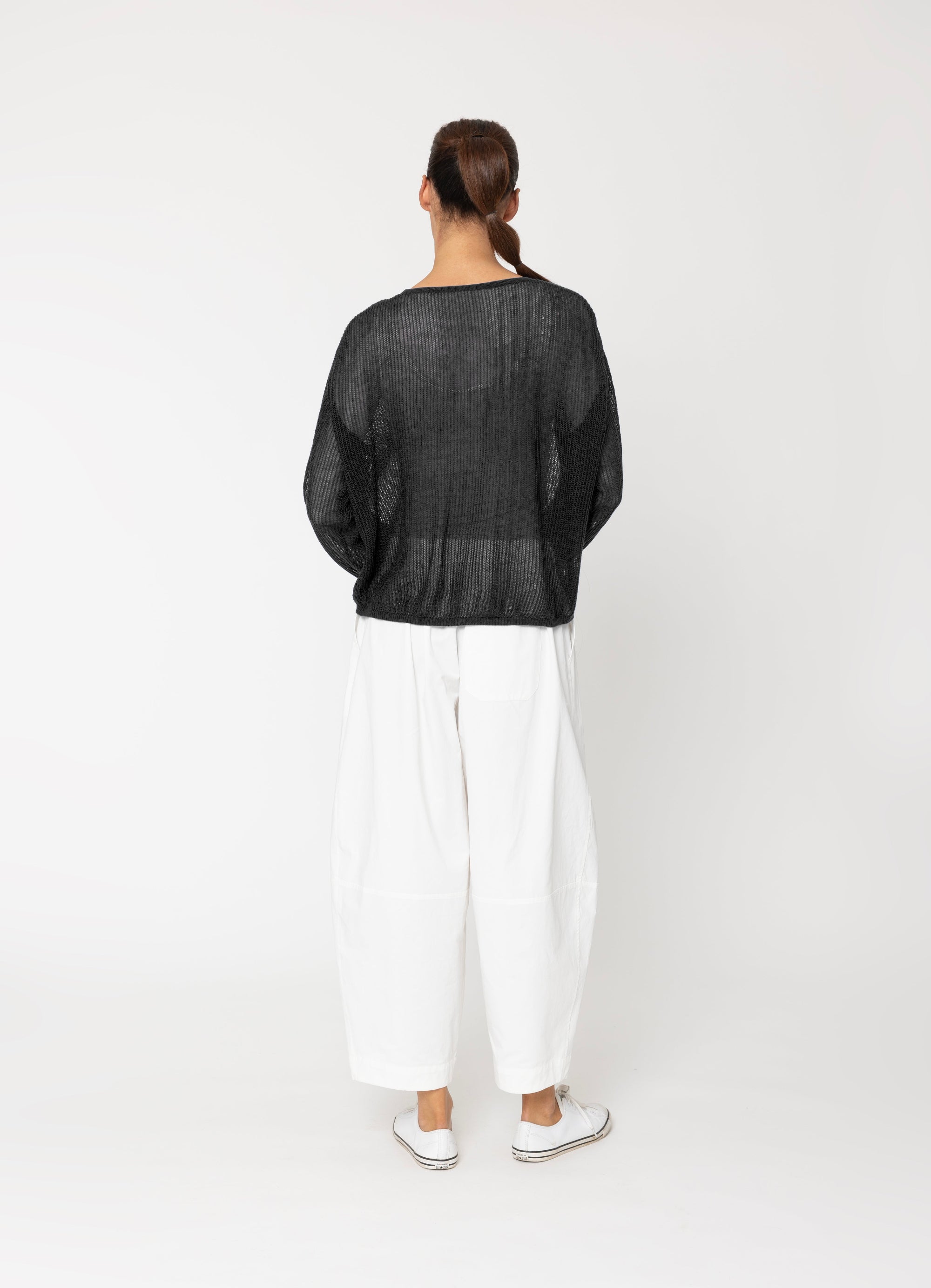 Person wearing a black jacket and white pants on a white background back angle