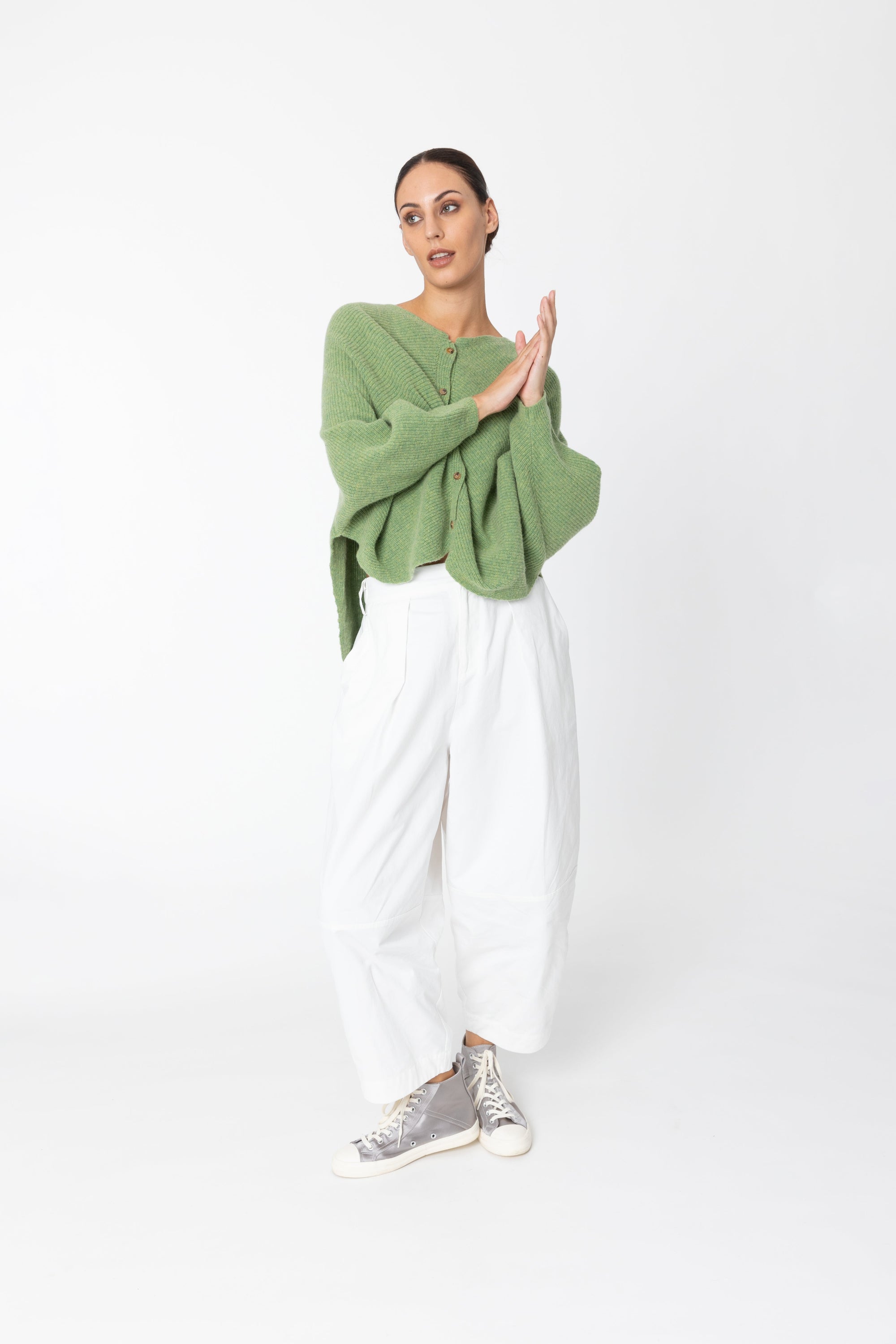 Woman wearing a green sweater and white pants on a white background