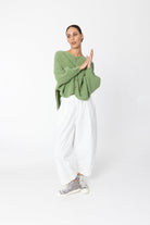 Woman wearing a green sweater and white pants on a white background