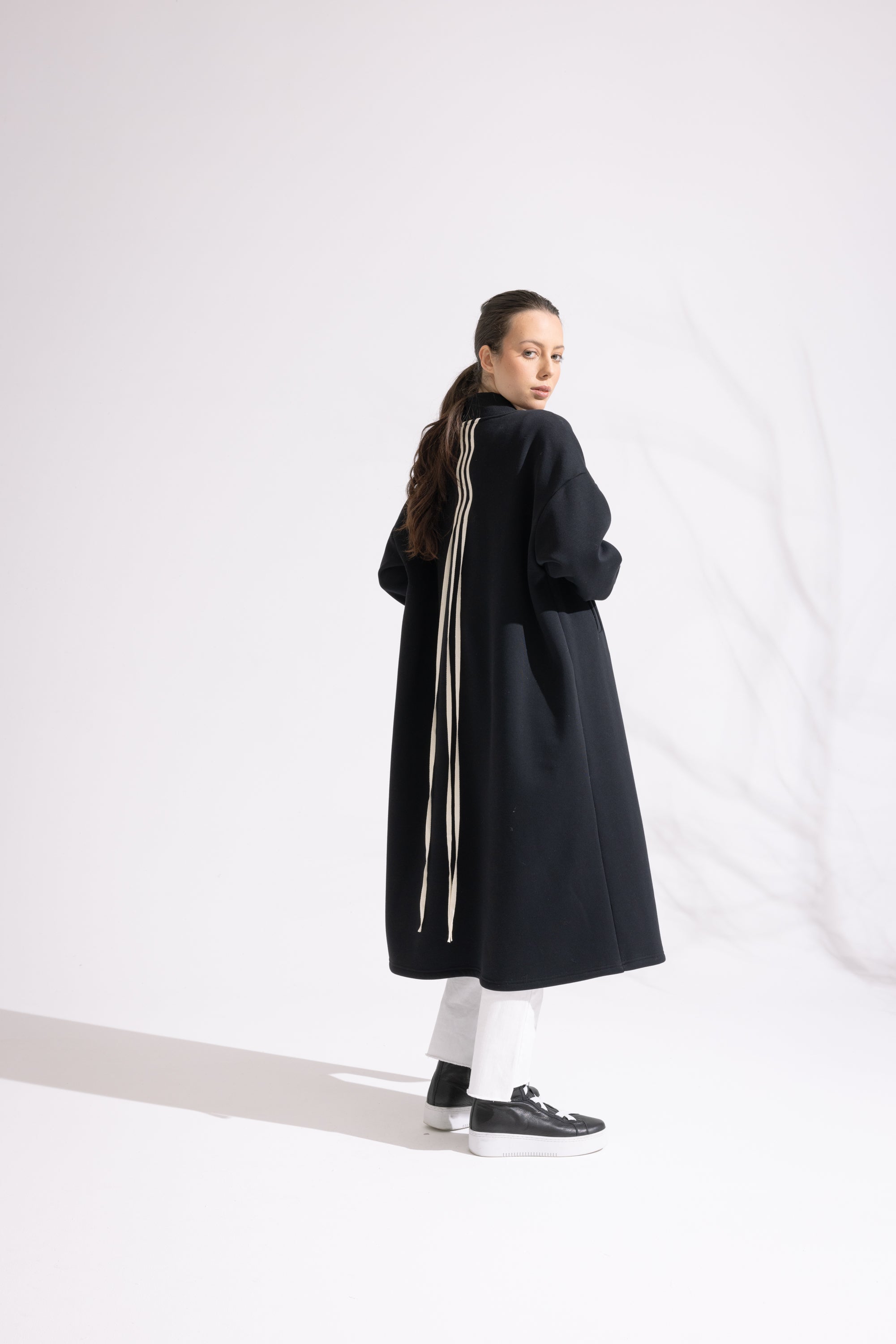 Person wearing a long black coat with white stripes on a white background