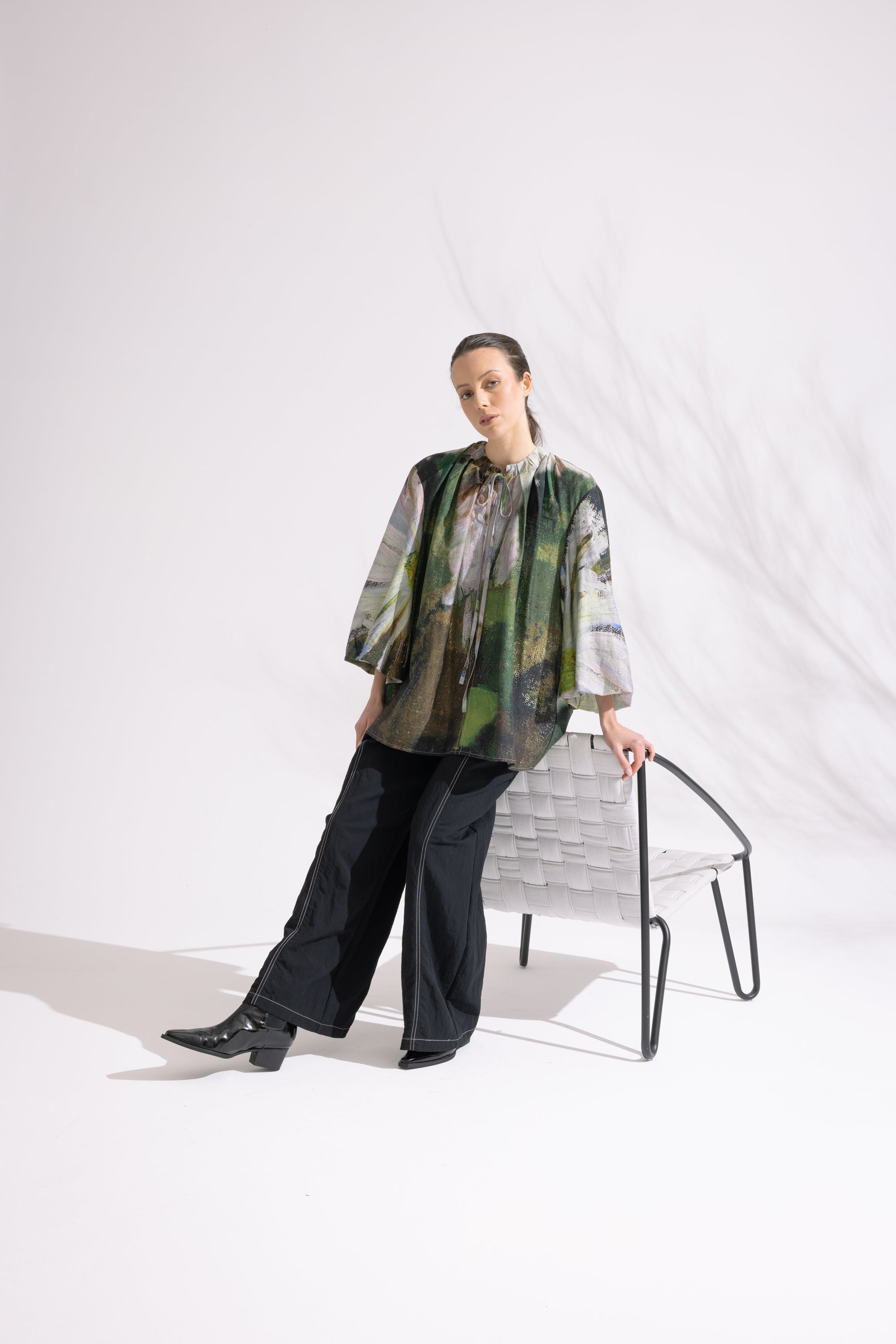 Person wearing a patterned shirt and black pants standing in a minimalistic setting.