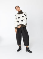 Person wearing a polka dot sweater and black pants on a white background