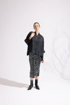 Person wearing a black jacket and patterned skirt on a white background