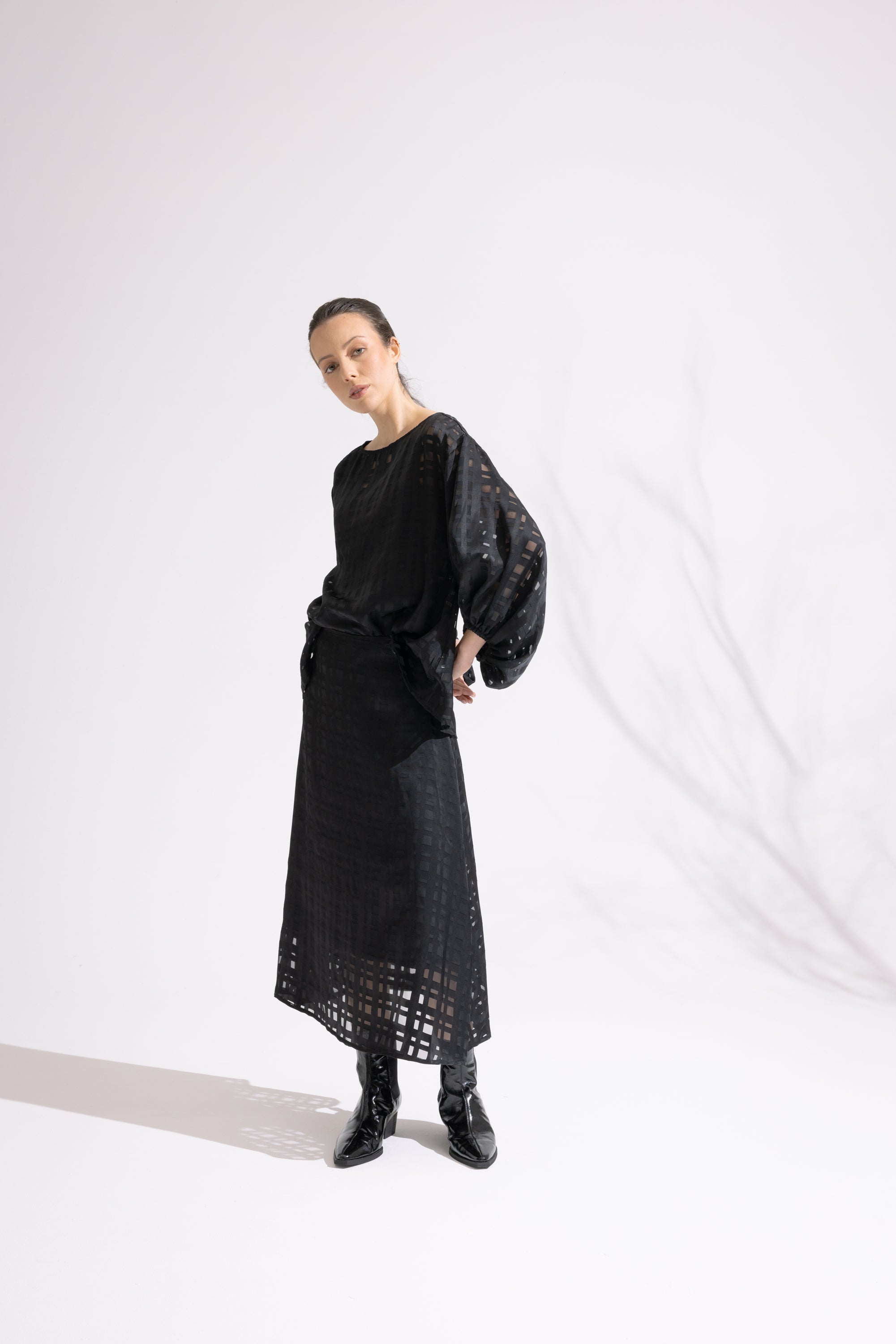 Person wearing a black outfit with a textured top and lace skirt against a white background