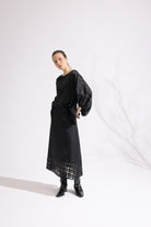 Person wearing a black outfit with a textured top and lace skirt against a white background