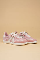 Pair of pink sneakers with white laces on a beige background