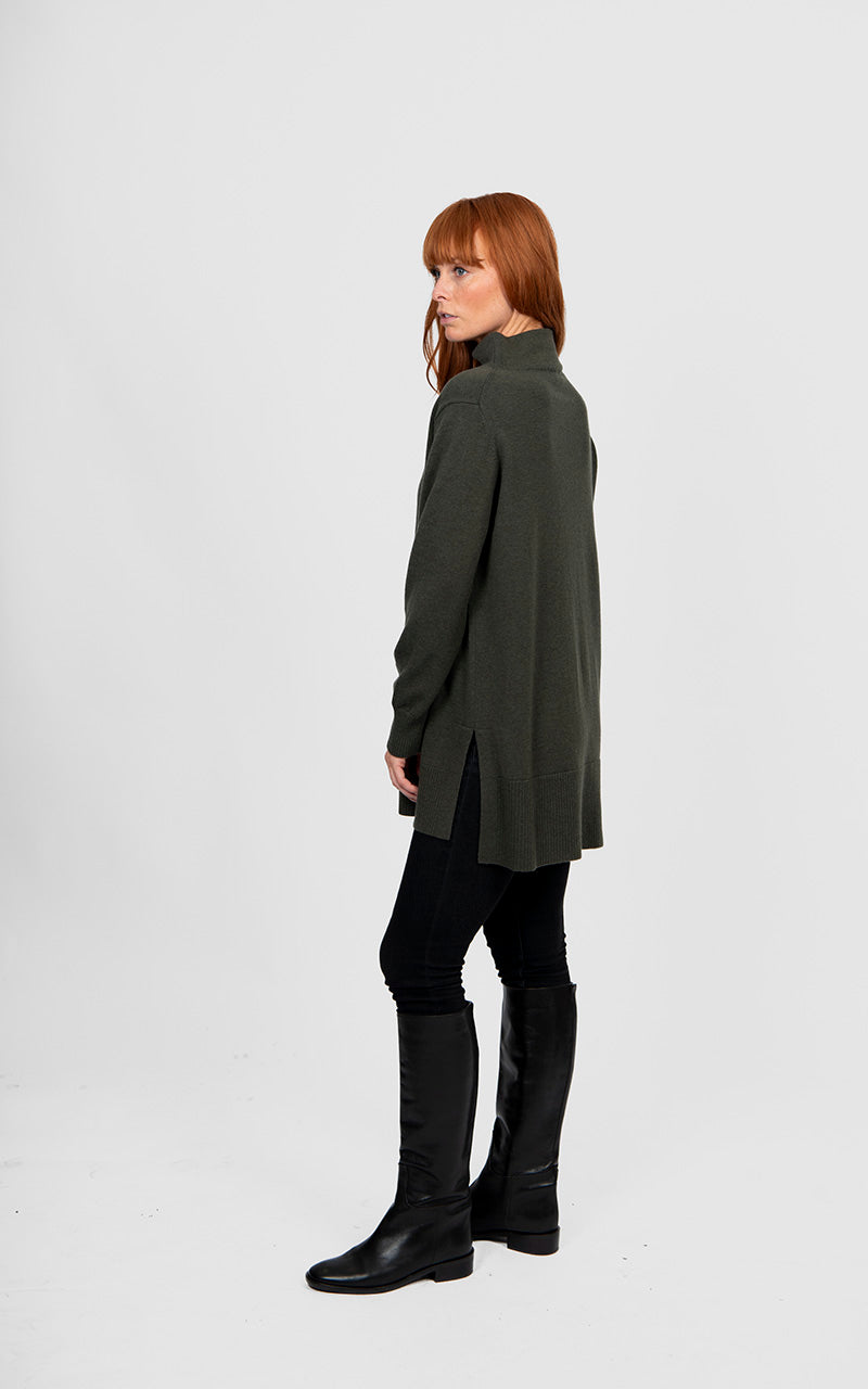 Person wearing a long green sweater and black boots on a white background