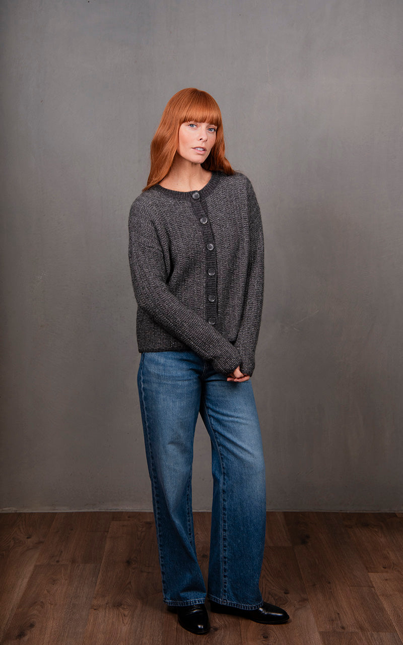 Woman wearing a dark gray cardigan and blue jeans against a plain background