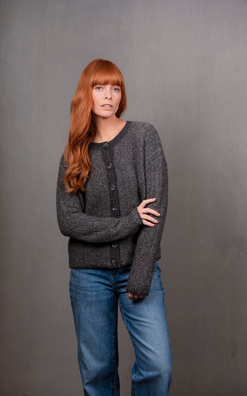 Woman wearing a gray knitted cardigan and blue jeans against a gray background