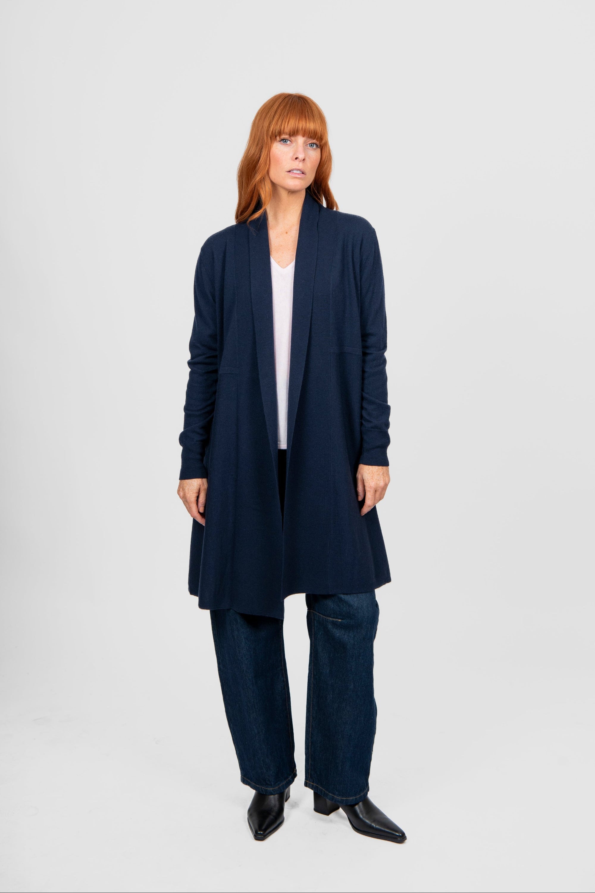 Woman wearing a long navy cardigan over a white top and dark pants on a light gray background