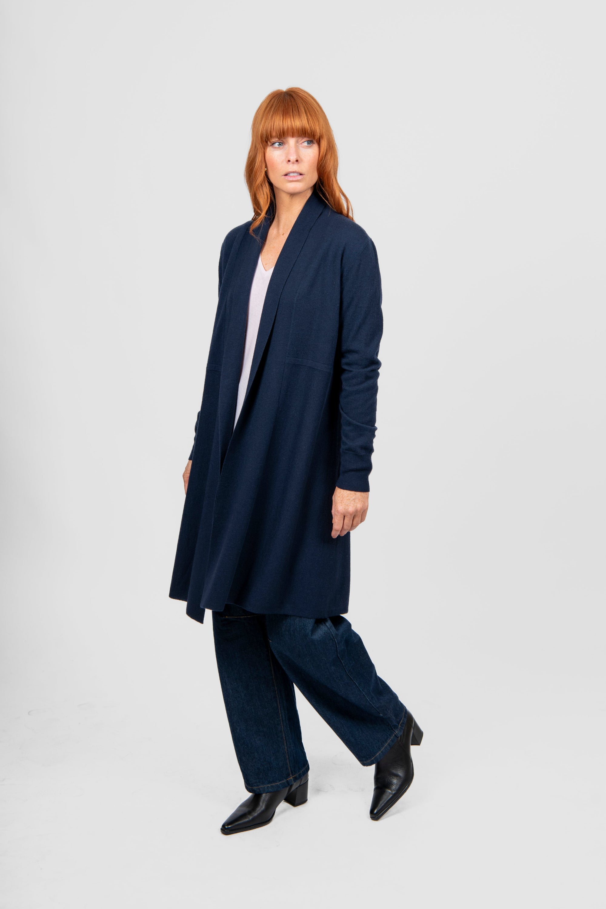 Woman wearing a long navy coat over a suit on a white background