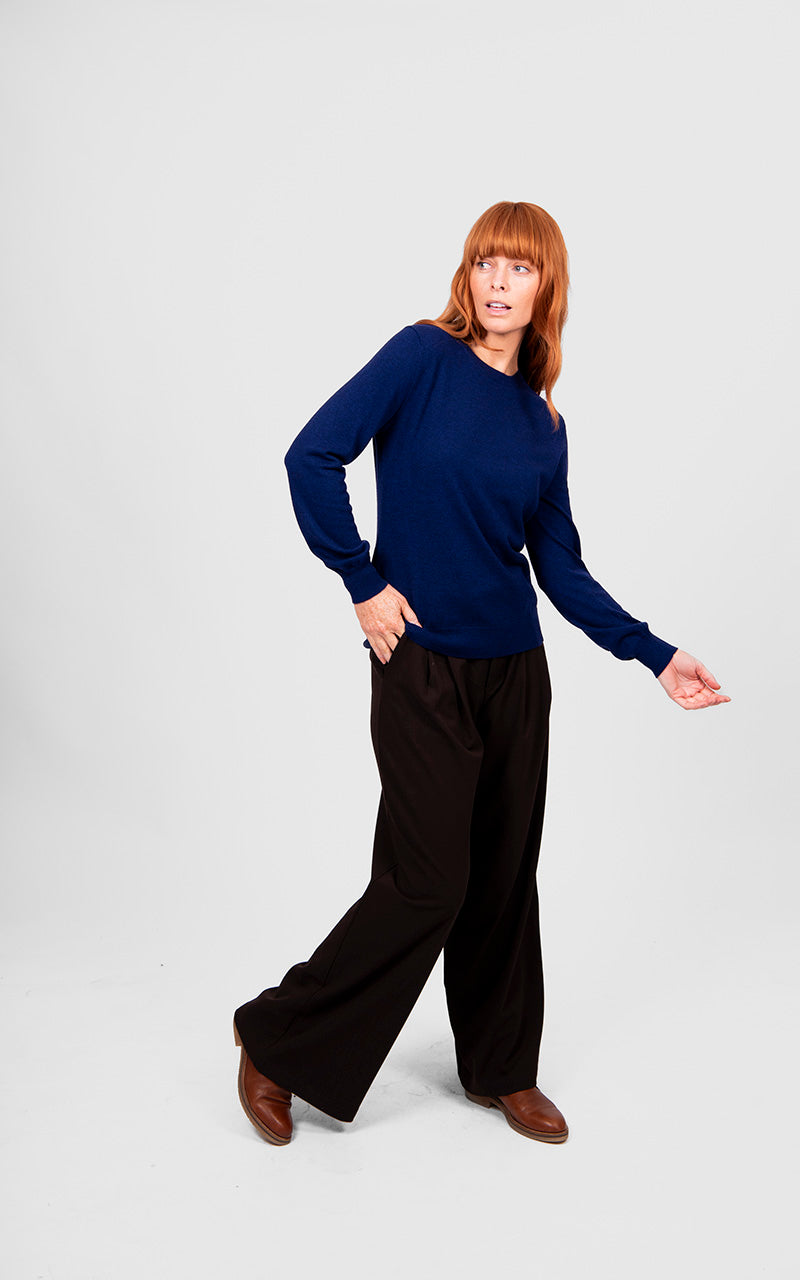 Woman wearing a navy sweater and black pants on a white background
