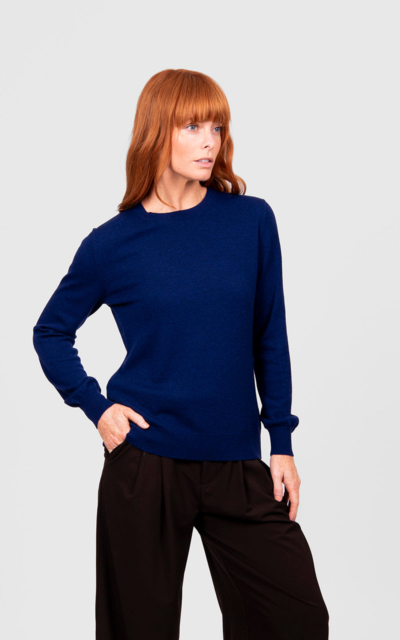 Woman wearing a blue sweater and black pants on a light gray background