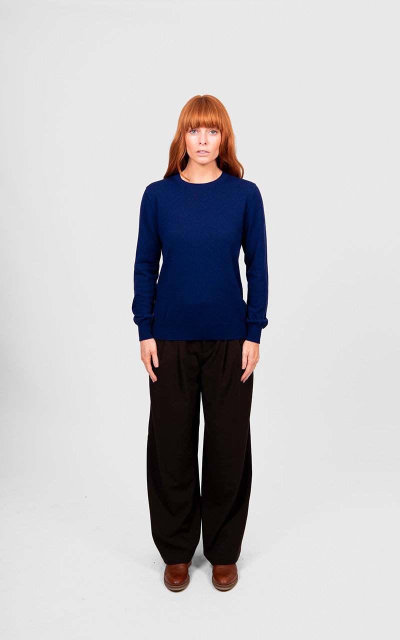 Person wearing a navy blue sweater and black pants on a white background