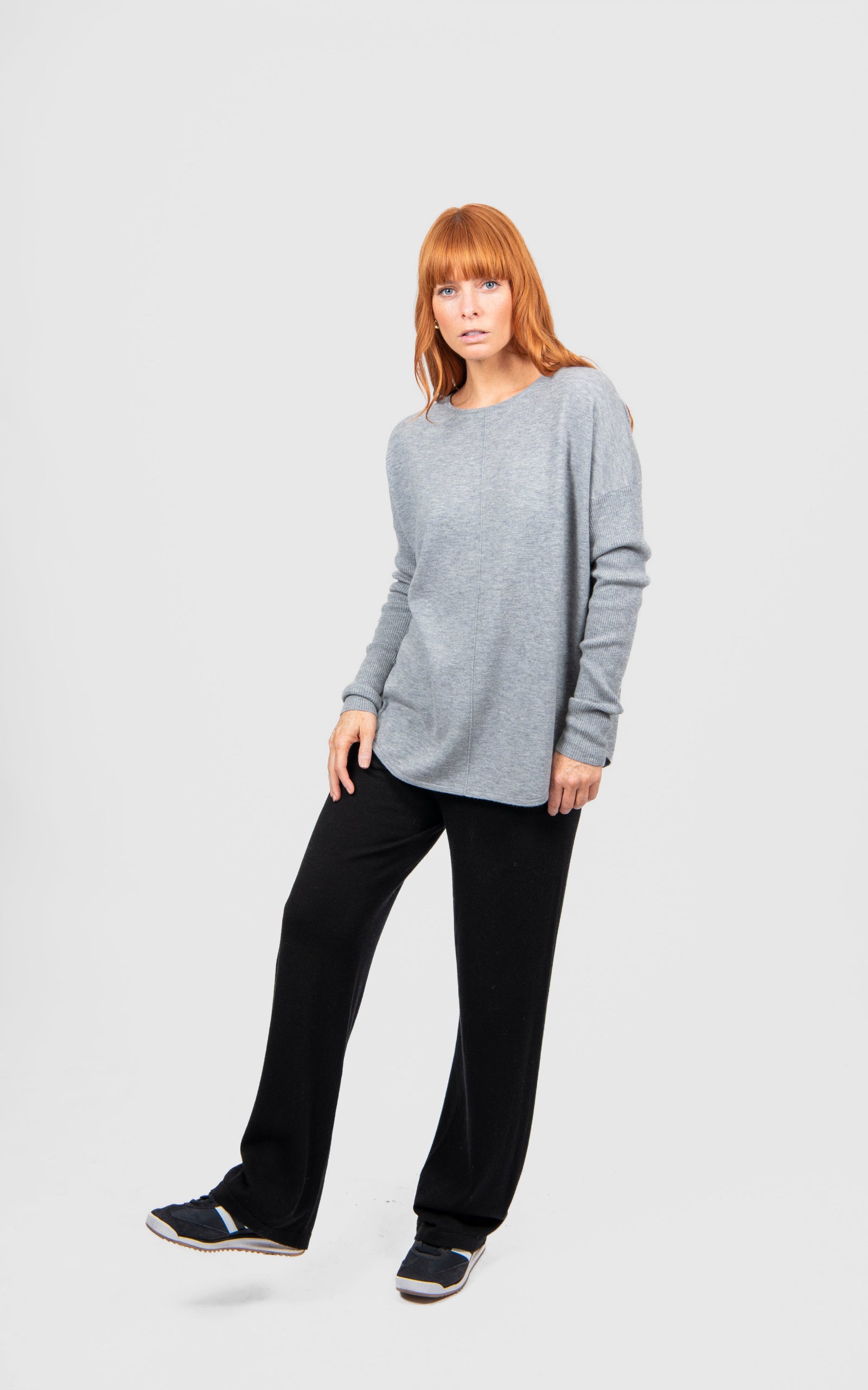 Woman wearing a gray sweater and black pants on a white background