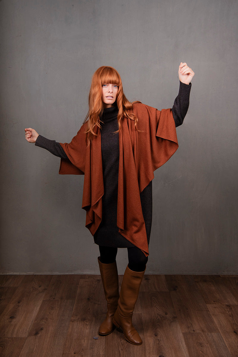 Woman wearing a brown poncho and boots against a gray background