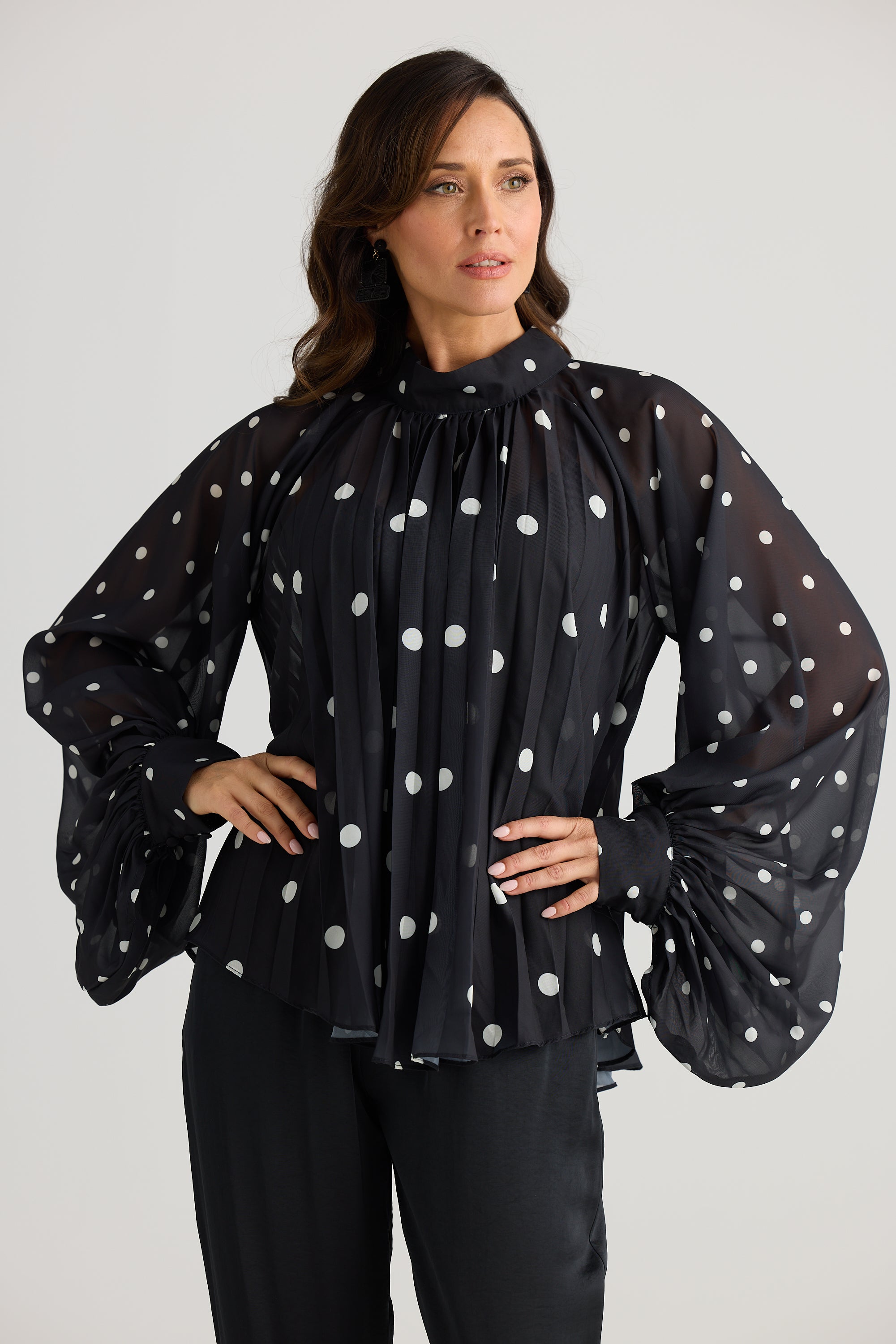 Woman wearing a black blouse with white polka dots on a plain background
