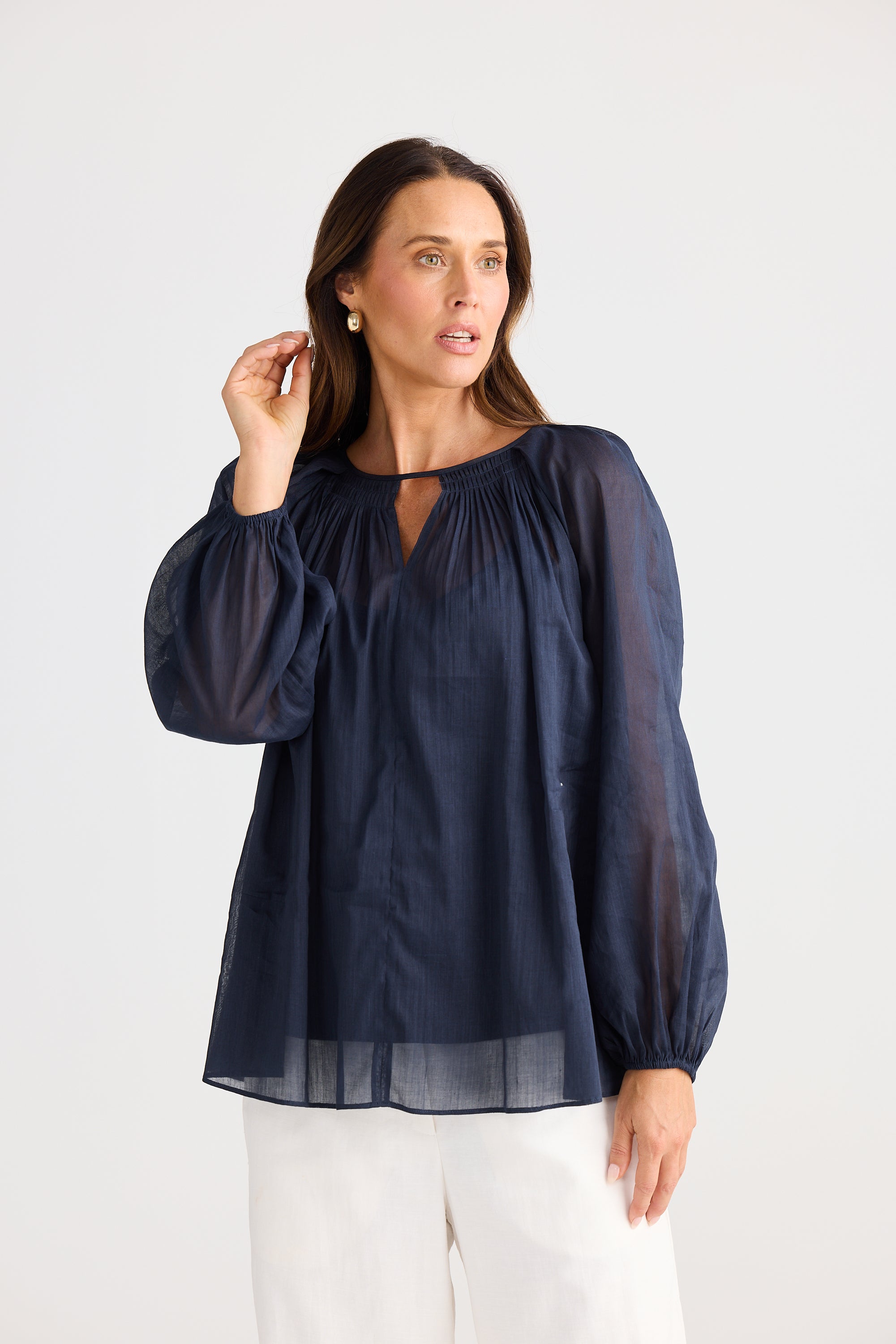 Woman wearing a navy blue blouse with sheer sleeves on a white background