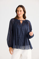 Woman wearing a navy blue blouse with sheer sleeves on a white background
